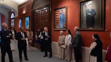 Group of formally dressed people in a museum hallway looking at large framed portraits on a red wall