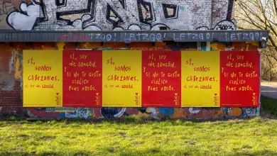Row of bright yellow and red posters on a graffiti wall, repeating the slogan 'Sí, somos de Aragón'.