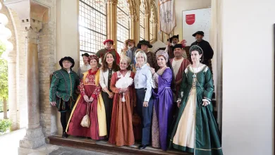 Group of people in colorful Renaissance costumes posing on a staircase inside a historic arched hall.