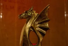 Golden dragon sculpture trophy in foreground with red neon 'SARQUSTA FILM FESTIVAL' sign in background