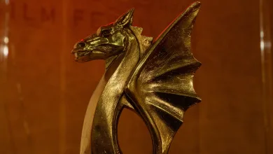 Golden dragon sculpture trophy in foreground with red neon 'SARQUSTA FILM FESTIVAL' sign in background