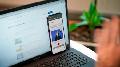 Laptop and smartphone on a desk; phone shows a video about Ibercaja videointerpretation service ('Servicio Ibercaja de videointerpretación').