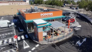 Aerial view of a Popeyes Louisiana Chicken restaurant with an orange sign, teal awnings, and an outdoor seating patio surrounded by a circular drive-through lane.