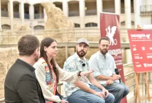 Panelists sitting in a row outdoors during a discussion, with red festival banners in the background and microphones visible on their shirts.