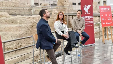 Three panelists sit on stools outdoors at a film festival discussion, with red festival banners in the background and rocky scenery behind them.