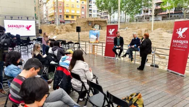 Panel discussion at Saraqusta Film Festival outdoors, with three speakers seated on stage and an audience. (informative)