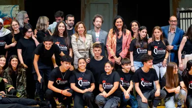 Group of diverse students posing on stage for a photo, many wearing black shirts with 'Premio Criticón' logos, smiles all around.