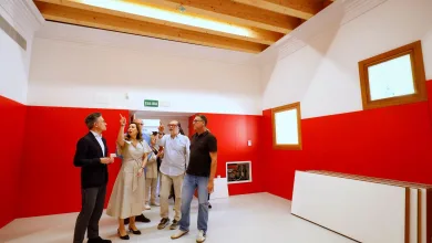 Group of professionals in a bright room with red lower walls and exposed wooden ceiling beams, one woman gesturing as others listen.
