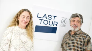 Two smiling people posing in front of a 'LAST TOUR' sign; woman on left wearing white lace top, man on right in patterned shirt.
