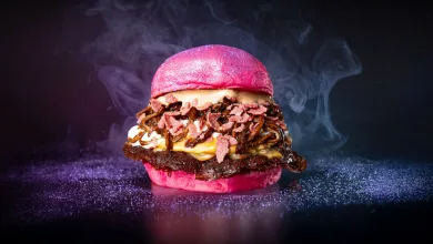Bright pink burger with bacon, melted cheese and crispy toppings on a pink bun against a dark background with purple dusting.