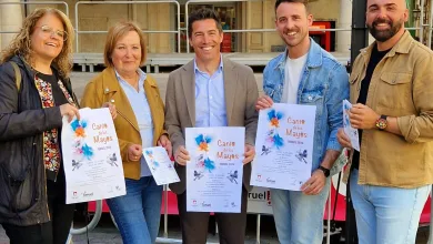 Five adults stand together outdoors, smiling, each holding a flyer for the 'Canto de los Mayos' event in Teruel 2026.