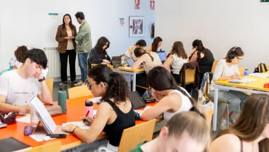 Group of Students Seated at Orange Tables Working on Laptops and Papers While Two Adults Stand Near the Wall in the Background Las Bibliotecas Del Actur Y Las Fuentes Abrirán Hasta Madrugada Durante Los Exámenes Zaragozala Qué Hacer En Zaragoza