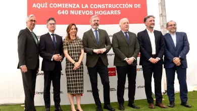 Siete personas en trajes formales posan frente a un cartel rojo que anuncia la construcción de 640 nuevos hogares en un acto oficial de inauguración
