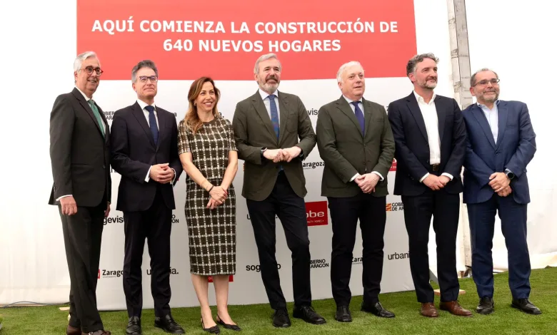 Siete personas en trajes formales posan frente a un cartel rojo que anuncia la construcción de 640 nuevos hogares en un acto oficial de inauguración