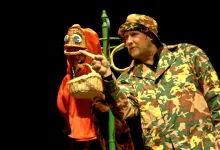Man in Camouflage Jacket and Hat Points Toward a Wicker Basket Puppet Wearing a Red Hood on a Dark Stage Background Zaragoza Qué Hacer En Zaragoza Zaragozala Qué Hacer En Zaragoza