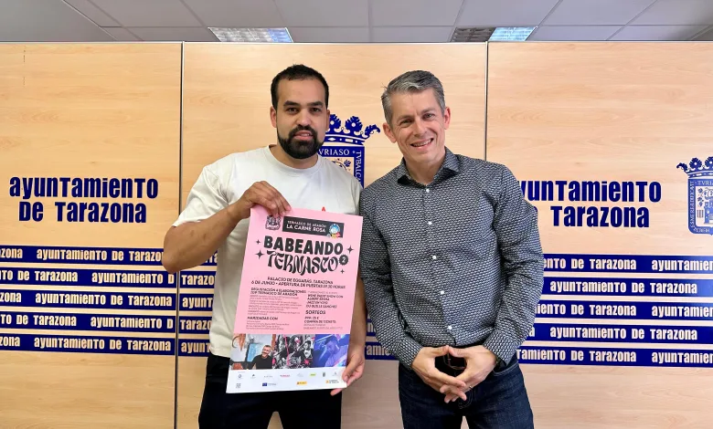 Two Men Smile for the Camera in Front of a Tarazona City Hall Backdrop the Man on the Left Holds a Pink Event Poster Tarazona Acoge babeando Ternasco El 6 De Junio Zaragozala Qué Hacer En Zaragoza