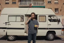 Man in a Gray T shirt Stands Beside a White Camper Van in a Parking Lot Eating an Orange Snack and Holding a Yellow Mug Zaragoza Qué Hacer En Zaragoza Zaragozala Qué Hacer En Zaragoza