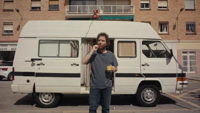 Man in a Gray T shirt Stands Beside a White Camper Van in a Parking Lot Eating an Orange Snack and Holding a Yellow Mug Zaragoza   Qué Hacer En Zaragoza Zaragozala   Qué Hacer En Zaragoza