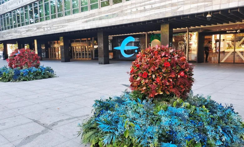 Urban Plaza in Front of a Modern Building with Glass Windows and a Blue Ibercaja Logo Colorful Flower Planters in the Foreground Ibercaja Transforma Plaza Paraíso Con Un Gran Jardín Floral Por Zaragoza Florece Zaragozala Qué Hacer En Zaragoza