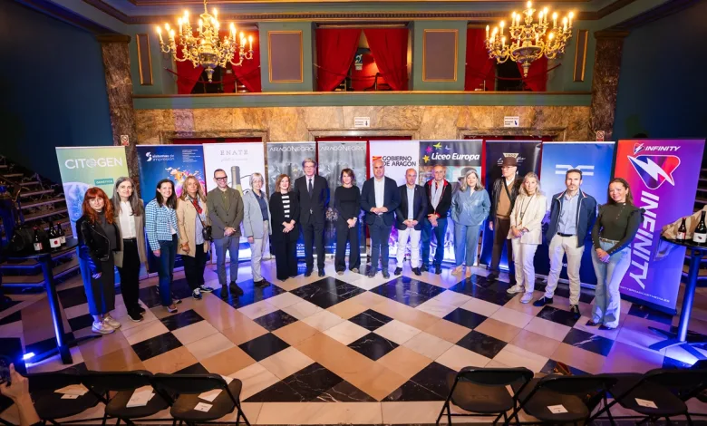 Group of professionals posing in a marble-floored venue with sponsor banners and chandeliers overhead.