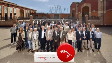Group of about 40 people posing outdoors for a formal photo in front of a building, with a white banner and red circular logo reading Somontano.