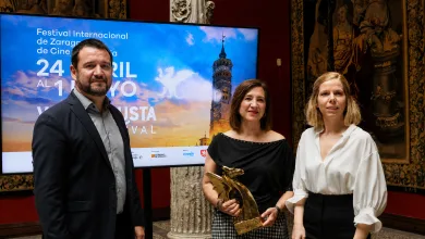 Three adults stand together at an award event, with a large screen behind them advertising the Festival Internacional de Zaragoza de Cine.