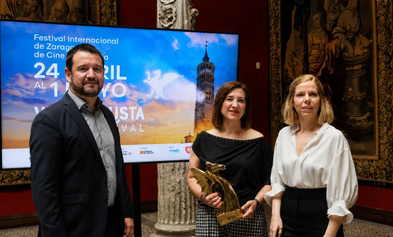 Three adults stand together at an award event, with a large screen behind them advertising the Festival Internacional de Zaragoza de Cine.