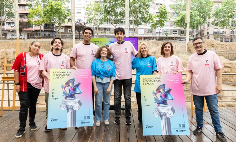 Eight people pose outdoors holding colorful event posters for I Jornadas de Pensamiento Clásico, with a construction site and trees in the background.