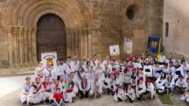 Group of Dancers in White Traditional Costumes with Red Sashes Pose in Front of a Historic Stone Building with Arches and Banners Nearby Veruela Reúne Los Dances Del Moncayo En Veruela Estival Zaragozala   Qué Hacer En Zaragoza