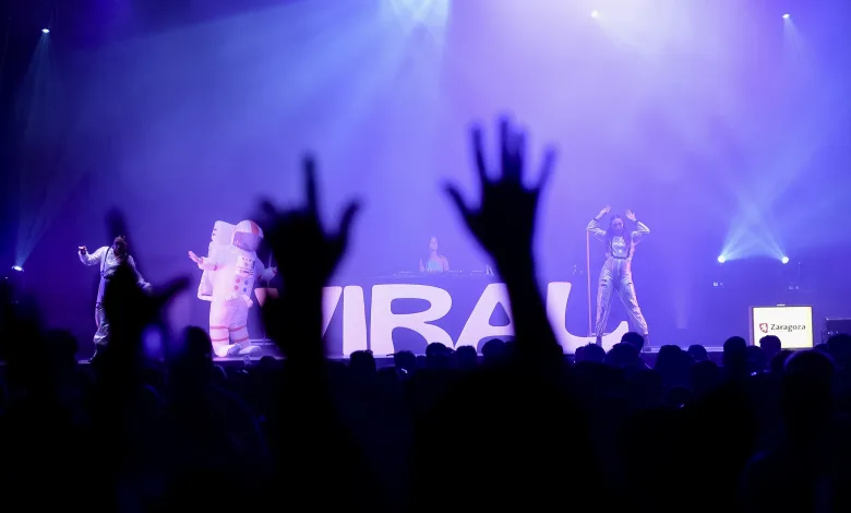 Concert Stage with Performers in Space themed Costumes Under Blue purple Lights Audience Hands Raised in the Foreground Large Letters on Backdrop Zaragoza Signage Visible La Fiesta Viral Light Repite En Las Fiestas Del Pilar 2026 Zaragozala   Qué Hacer En Zaragoza