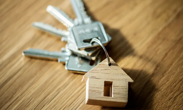 Key Ring with a Metal House shaped Wooden Tag on a Wood Surface in the Background Alquiler Asequible Zaragoza Así Optar a 78 Viviendas Zaragozala Qué Hacer En Zaragoza
