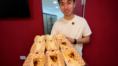 Young Man in a White T shirt Stands Behind a Table Displaying Multiple Opened Pizza Boxes Arranged Like Wedges on a Counter in a Red walled Room 99cheesecake Llega a Calle Alfonso En Pleno Auge De Las Tartas De Queso Zaragozala Qué Hacer En Zaragoza