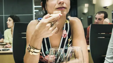 Woman in a Floral Dress Bringing a Bite of Food to Her Lips at a Table in a Restaurant with Two Wine Glasses in the Foreground and Other Diners in the Background Bus Del Vino Somontano Ruta Dulce Y Vino El 27 De Junio Zaragozala   Qué Hacer En Zaragoza