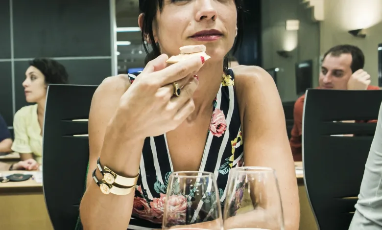 Woman in a Floral Dress Bringing a Bite of Food to Her Lips at a Table in a Restaurant with Two Wine Glasses in the Foreground and Other Diners in the Background Bus Del Vino Somontano Ruta Dulce Y Vino El 27 De Junio Zaragozala Qué Hacer En Zaragoza