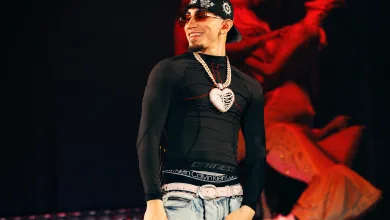 Male Performer on Stage Wearing a Black Fitted Shirt Light Jeans with a White Belt a Bandana Sunglasses and a Large Heart Pendant Necklace While Holding a Pink Microphone Concierto De Omar En Zaragoza   Espacio Zity 2026 Zaragozala   Qué Hacer En Zaragoza