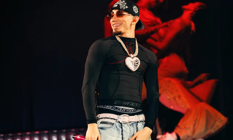 Male Performer on Stage Wearing a Black Fitted Shirt Light Jeans with a White Belt a Bandana Sunglasses and a Large Heart Pendant Necklace While Holding a Pink Microphone Concierto De Omar En Zaragoza   Espacio Zity 2026 Zaragozala   Qué Hacer En Zaragoza
