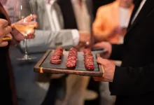 Tray of Small Raw Meat Skewers on a Wooden Board at a Social Gathering with Blurred Guests and a Wine Glass in the Background Zaragozala | Agenda Cultural Ocio Y Planes En Zaragoza Zaragozala   Qué Hacer En Zaragoza
