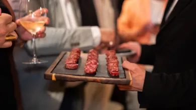 Tray of Small Raw Meat Skewers on a Wooden Board at a Social Gathering with Blurred Guests and a Wine Glass in the Background Fiesta De La Longaniza De Graus Busca Reconocimiento Nacional Zaragozala   Qué Hacer En Zaragoza
