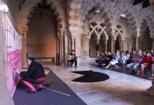 Guitarist Seated on Stage Playing a Guitar in a Historic Arched Hall with an Audience Seated and Watching a Performance Zaragozala | Agenda Cultural Ocio Y Planes En Zaragoza Zaragozala Qué Hacer En Zaragoza