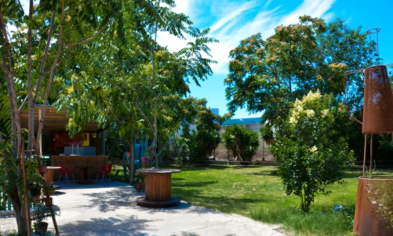 Sunny Outdoor Garden with Tall Trees a Paved Path a Wooden Spool Table and a Rust Sculpture on the Lawn to the Right Under a Blue Sky El Público a Escena Se Traslada Al Espacio Cirteani En Julio Zaragozala   Qué Hacer En Zaragoza