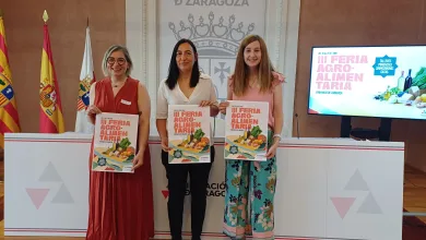 Three Women Stand Side by Side Each Holding a Brochure for a Regional Fair in a Formal Presentation Room with Flags and a Screen to the Right Feria Agroalimentaria De Zaragoza En El Palacio De Sástago Zaragozala Qué Hacer En Zaragoza