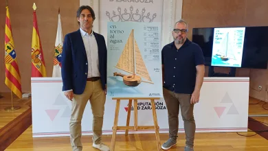 Two Men Stand Beside a Poster on an Easel at a Formal Event About Water El Ciclo Entorno Al Agua 2026 Ofrece Seis Conciertos Gratis Zaragozala Qué Hacer En Zaragoza