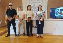 Four Adults Stand in a Row Indoors at a Diputación De Zaragoza Setting Each Holding a Brochure and Smiling at the Camera with a Spanish Flag and a Screen in the Background Zaragozala | Agenda Cultural Ocio Y Planes En Zaragoza Zaragozala   Qué Hacer En Zaragoza