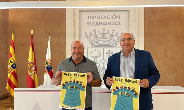 Two Men in a Formal Setting Hold Bright Posters in Front of the Zaragoza Provincial Council Emblem and Flags in the Background Festival Orés Mágico 2026 Información Y Actividades Zaragozala Qué Hacer En Zaragoza