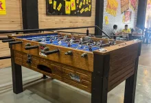 Indoor Foosball Table with a Wooden Finish and Black Legs Players Are on the Rods in a Space with Yellow Posters on the Wall at the Back Zaragozala | Agenda Cultural Ocio Y Planes En Zaragoza Zaragozala   Qué Hacer En Zaragoza