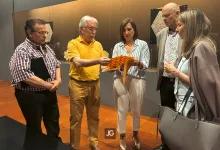 Five Adults Stand in an Exhibition Space As a Man in a Yellow Shirt Hands Orange Patterned Papers to a Woman in a Striped Blouse While Others Look On Zaragozala | Agenda Cultural Ocio Y Planes En Zaragoza Zaragozala Qué Hacer En Zaragoza