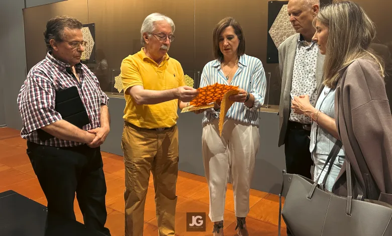 Five Adults Stand in an Exhibition Space As a Man in a Yellow Shirt Hands Orange Patterned Papers to a Woman in a Striped Blouse While Others Look On Viaje a Las Estrellas Exposición De Miguel Gañán En El Emoz Zaragozala Qué Hacer En Zaragoza