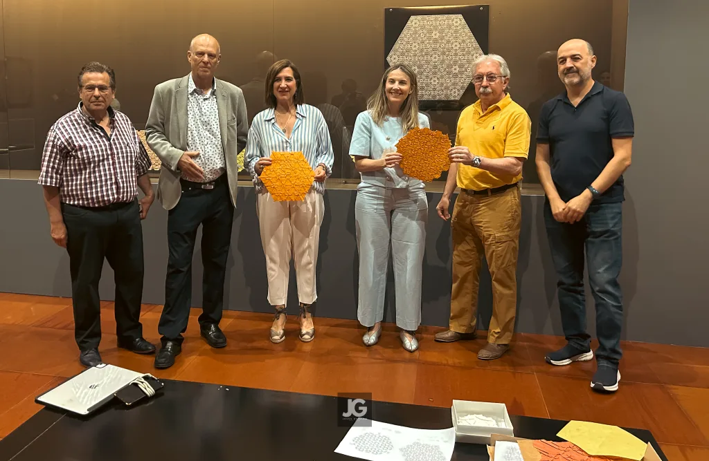 Six Adults Pose Together Indoors Two Women in the Middle Hold Orange Hexagonal Art Pieces with a Brown Wall and Display Behind Them Viaje a Las Estrellas Exposición De Miguel Gañán En El Emoz Zaragozala Qué Hacer En Zaragoza