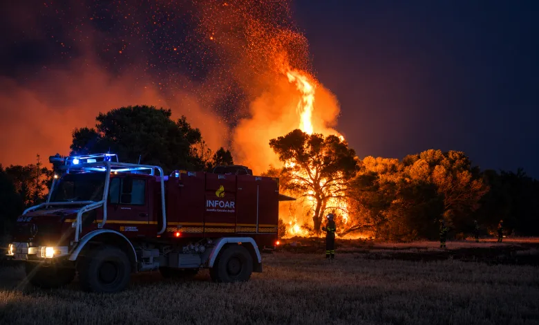 Night Scene of a Forest Fire with a Towering Blaze Behind Trees a Red Fire Truck with Blue Emergency Lights in the Foreground Firefighters on the Field Nearby Incendio En Leciñena Más De 1000 Hectáreas Afectadas Zaragozala   Qué Hacer En Zaragoza