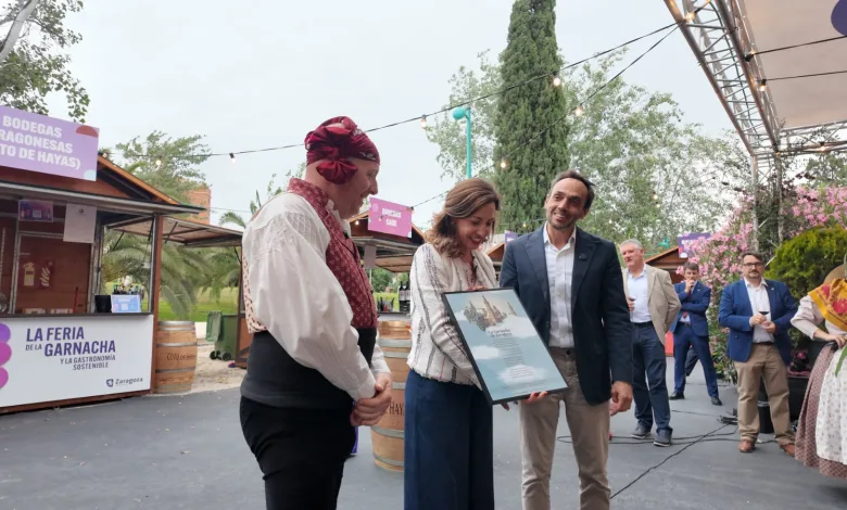 Woman in Traditional Dress Receives a Framed Certificate from Two Men at a Wine Festival with String Lights and Stalls in the Background Zaragozala | Agenda Cultural Ocio Y Planes En Zaragoza Zaragozala   Qué Hacer En Zaragoza